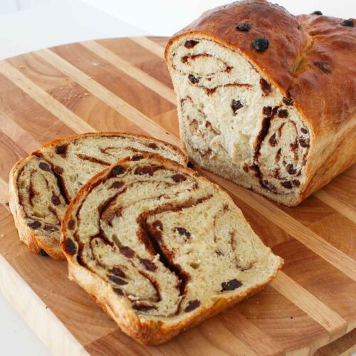 Two slices of cinnamon bread sit on a wooden cutting board with the remaining loaf sitting nearby.
