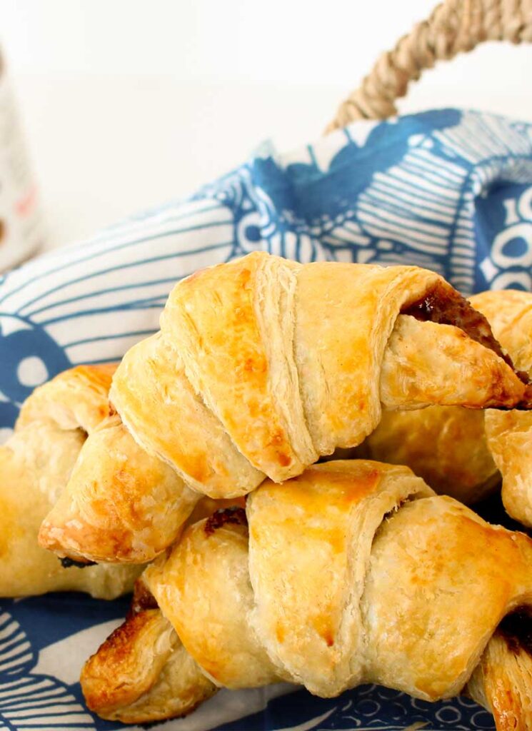 Homemade Nutella croissants are sitting in a basket lined with a blue napkin.