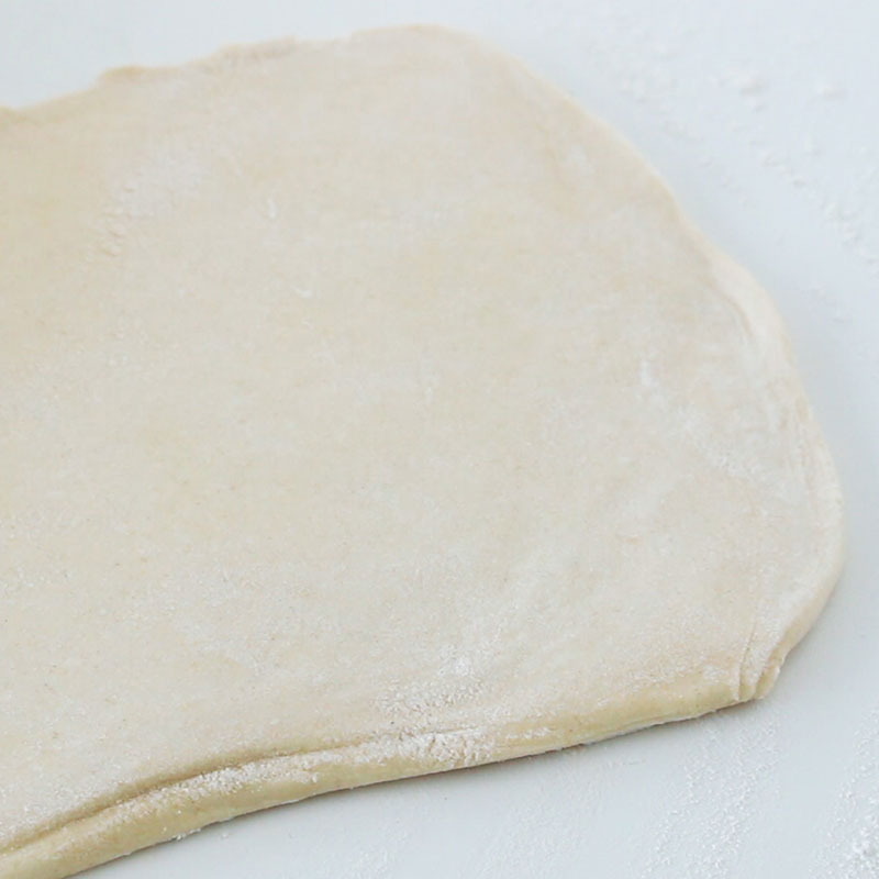 A sheet of puff pastry has been rolled out on a white, floured countertop.
