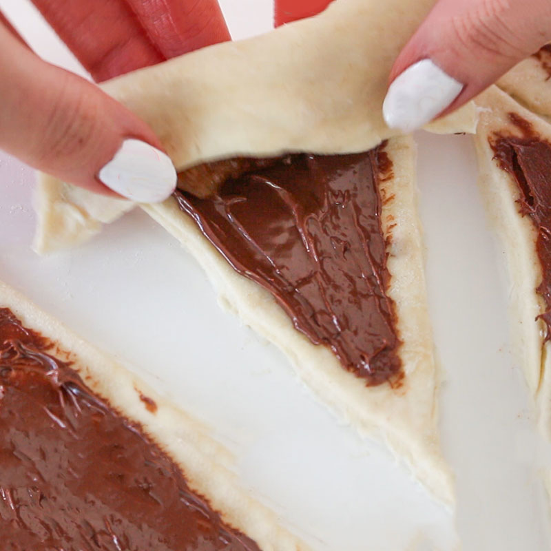 A triangle of dough is being rolled up, starting from the widest end.