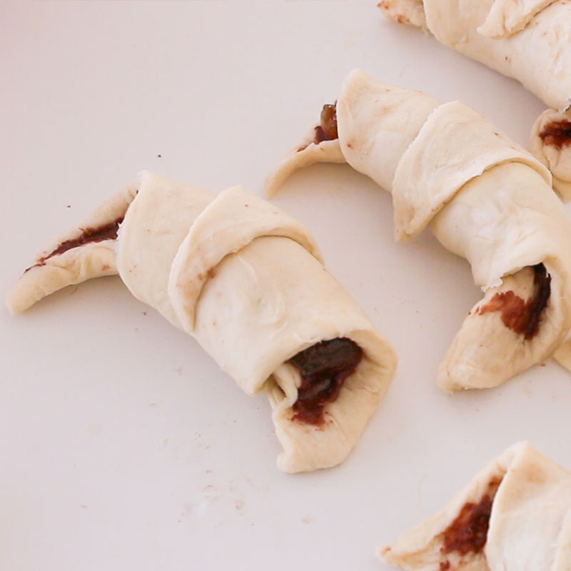 The croissants have been filled and rolled up. They are sitting on a white counter.