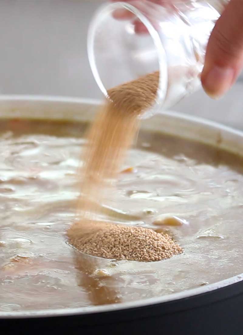 Japanese powdered bonito stock is being poured from a small glass into a pot of curry.