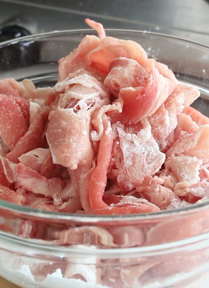 A glass bowl contains thinly sliced pork that has been coated in potato starch.