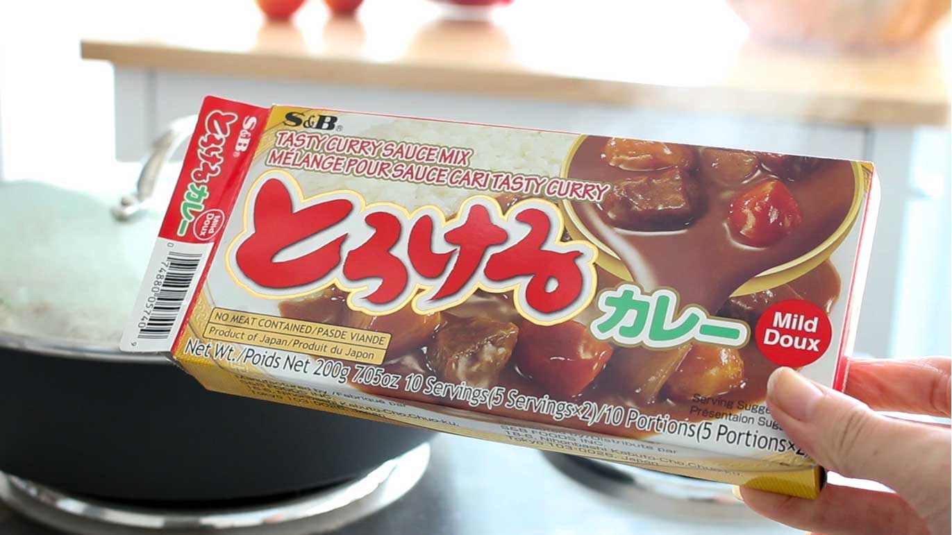 A hand is holding up a box of Japanese curry paste, called Torokeru Curry.