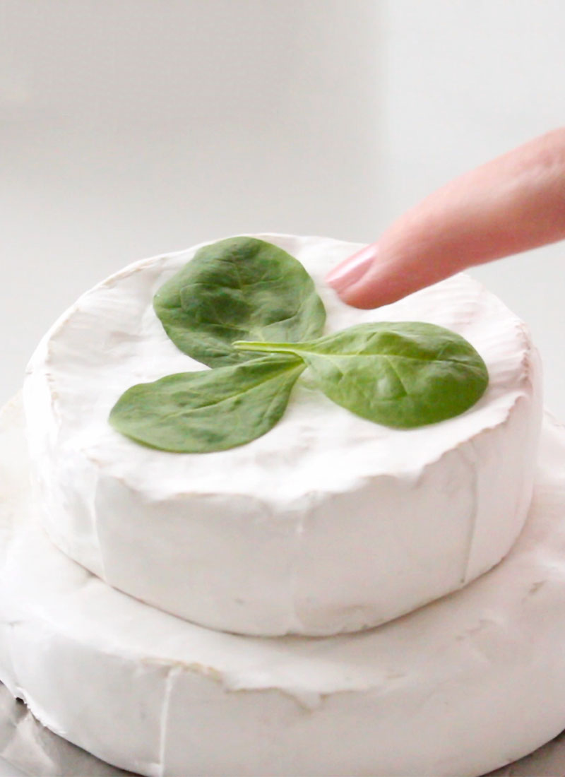 a finger placing spinach leaves on top of brie cheese