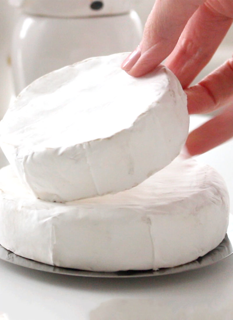 a wheel of brie being stacked on top of a larger wheel of brie cheese