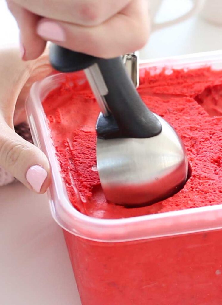 A hand is using an ice cream scoop to take a scoop out of some freshly frozen red velvet ice cream.