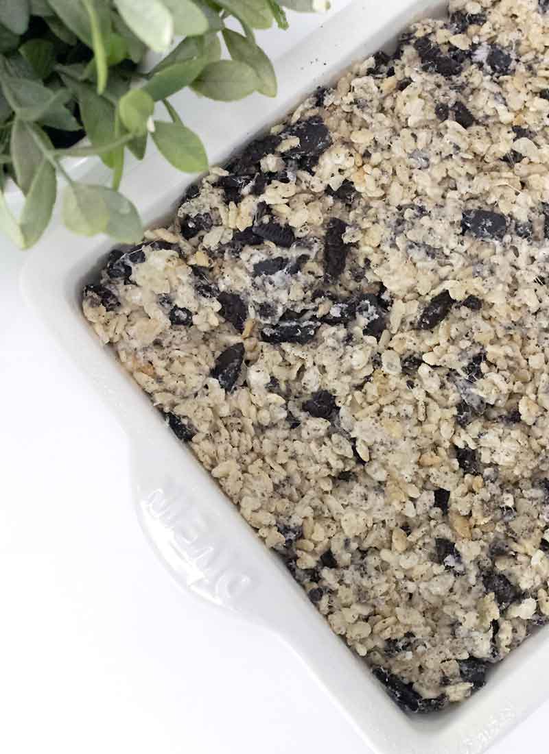 cereal treats in a white baking dish on a white tabletop with a green plant nearby.