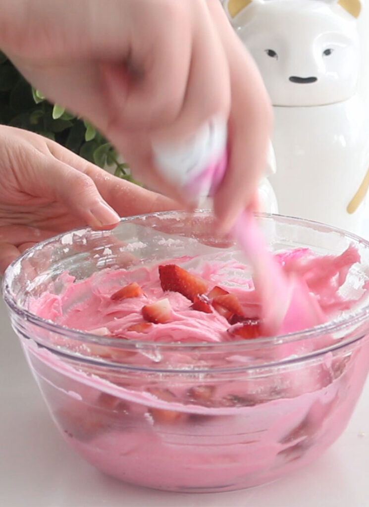 Fresh diced strawberries are being folded into pink cake batter with a spatula.