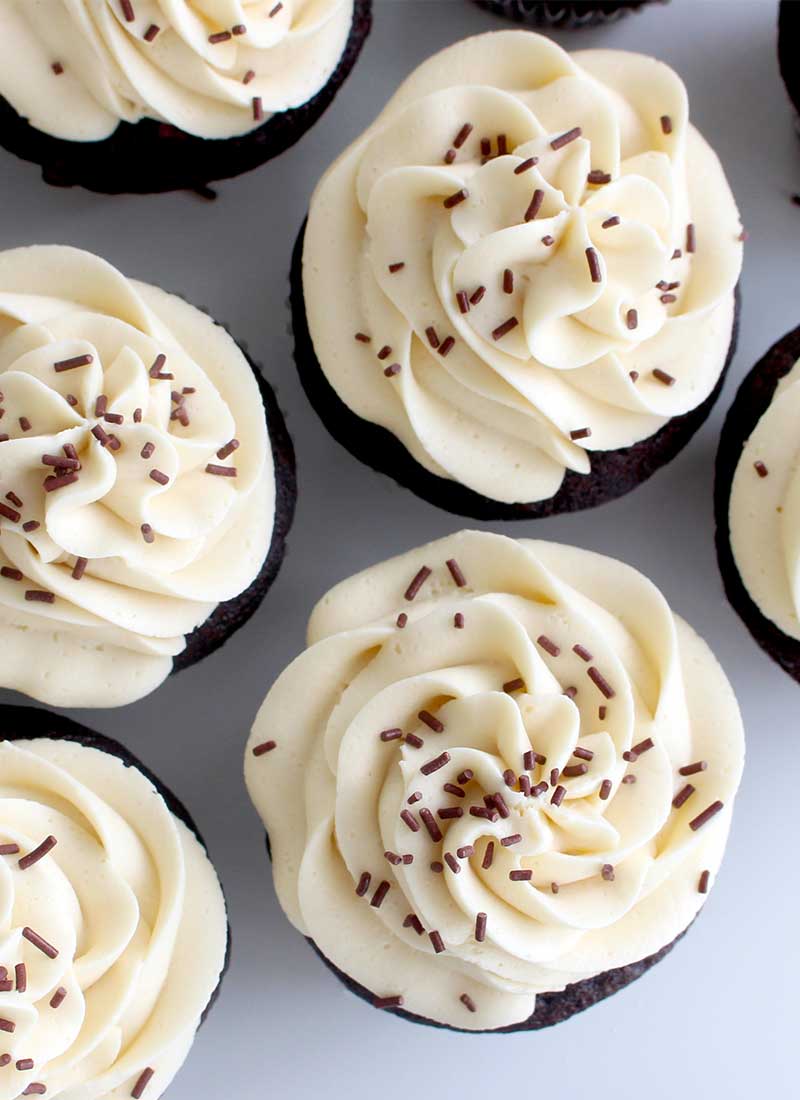 chocolate cupcakes with white frosting and chocolate sprinkles, on a white table top