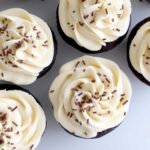 chocolate cupcakes with white frosting and chocolate sprinkles, on a white table top