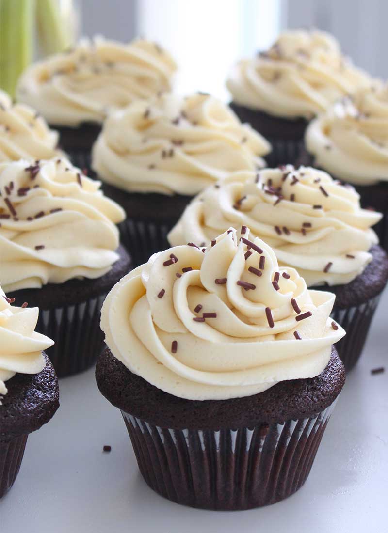 chocolate cupcakes with white frosting and chocolate sprinkles, on a white table top