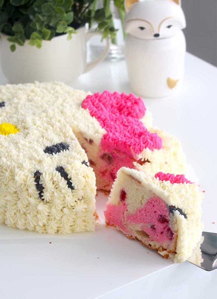 A slice has been cut of the cake and is being lifted from the cake with a cake server. The inside of the cake is a pink and white marble.