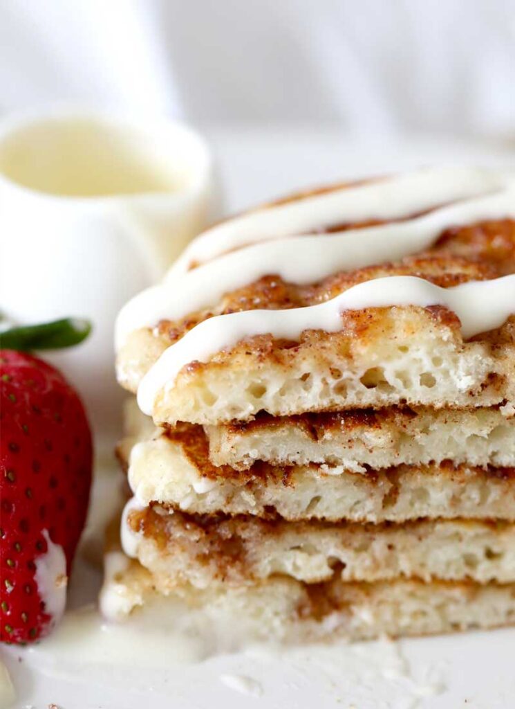 A close up of a stack of pancakes that has been cut in half. The pancakes have been drizzled with cream cheese glaze.