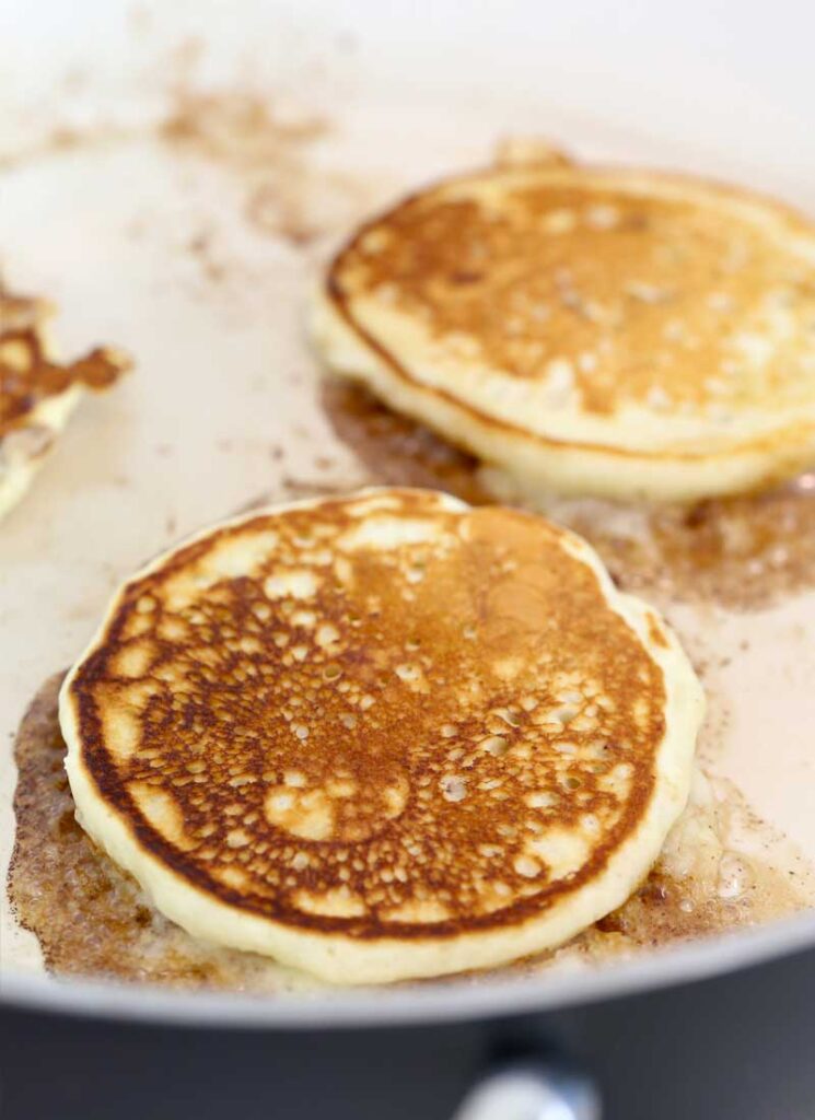 Two pancakes in a frying pan. They have been flipped and are golden brown.