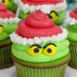 A cupcake decorated to look like the character, the Grinch, from the movie How the Grinch Stole Christmas.