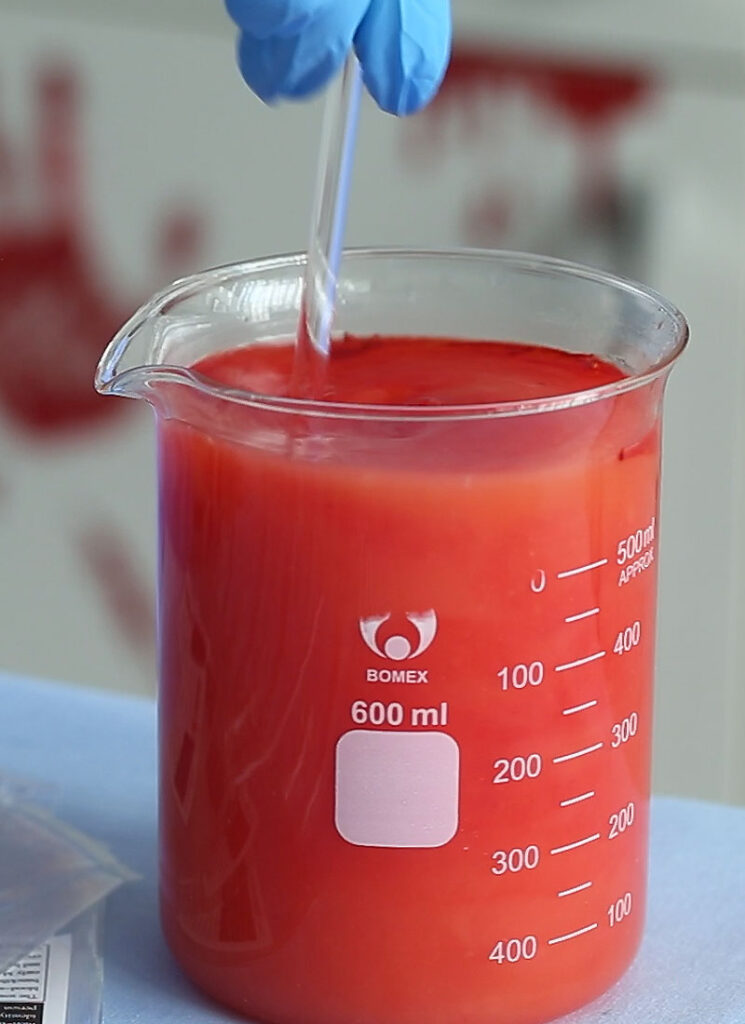 Red juice in a glass beaker being stirred with a glass stir stick.