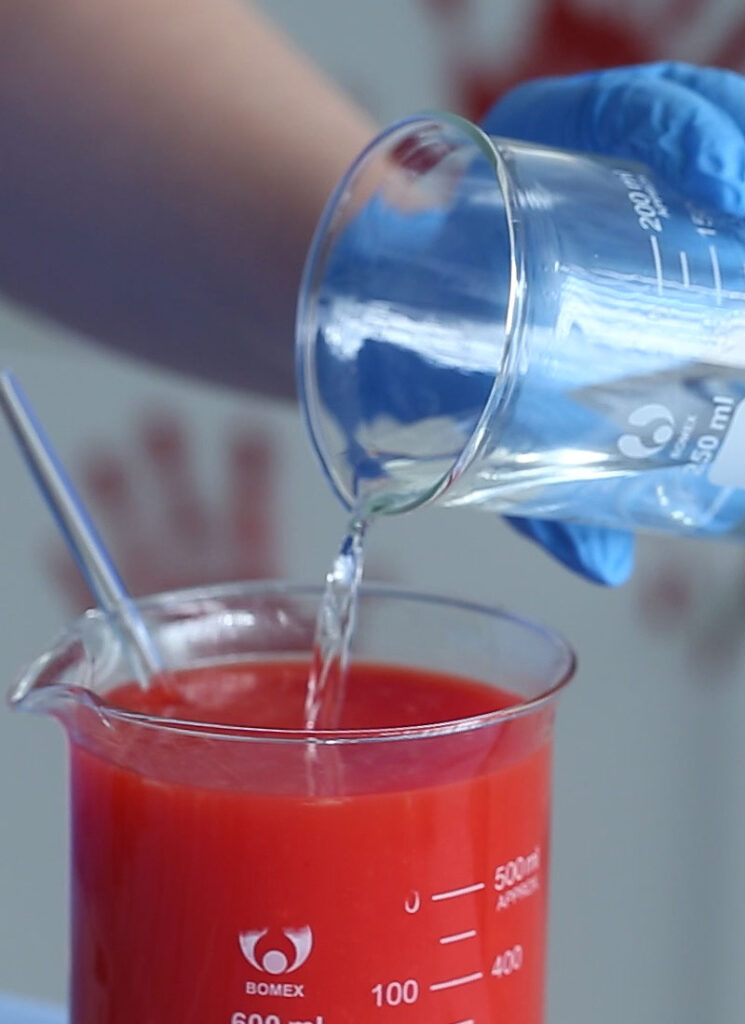 Vodka is being poured into a glass beaker filled with red juice.