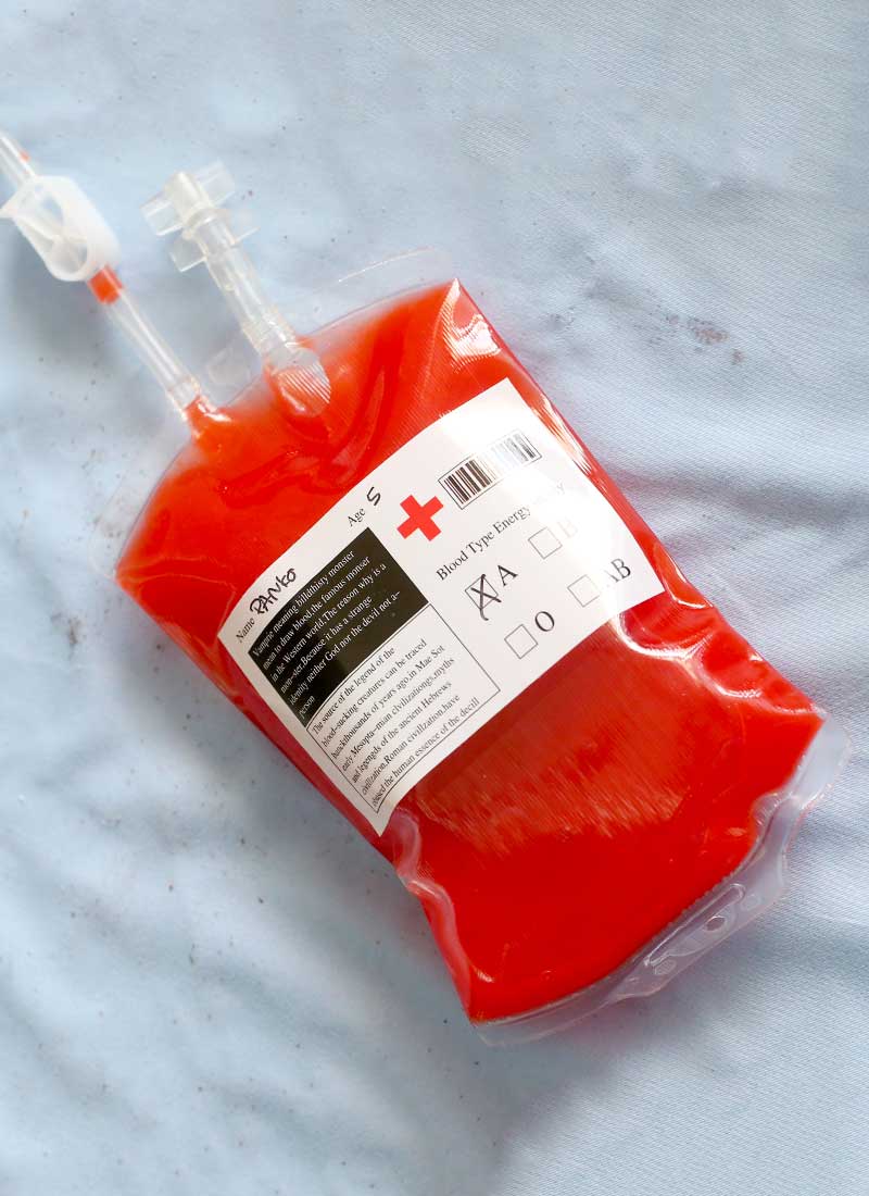 One iv drink bag is filled with red punch on a blue cloth background.