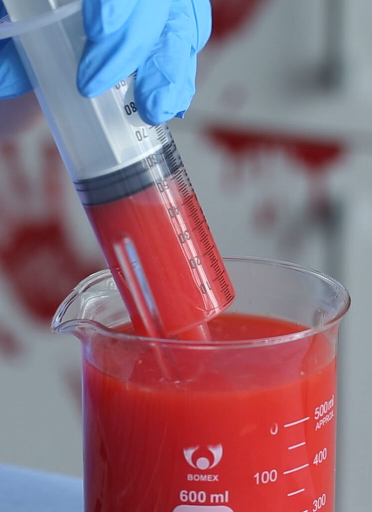 A large syringe is being used to draw up red cocktail from a glass beaker.