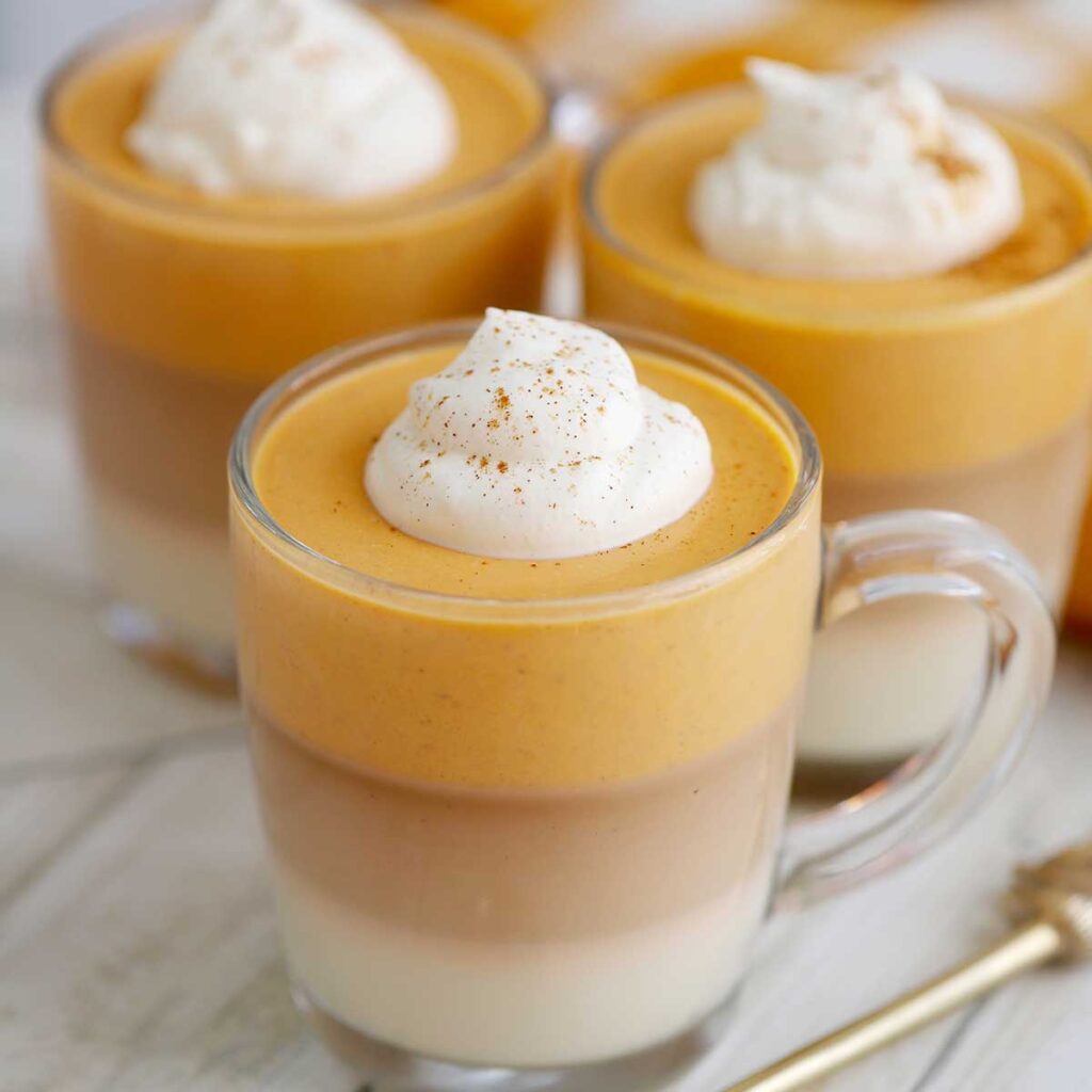 Glasses of layered panna cotta are sitting on a wooden table, topped with dollops of whipped cream.