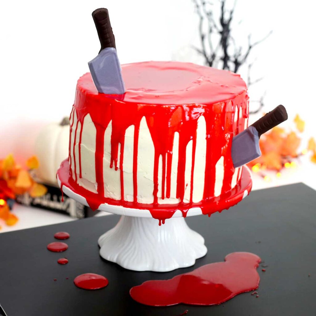 a white cake dripping with blood chocolate ganache, with chocolate knives stuck into it
