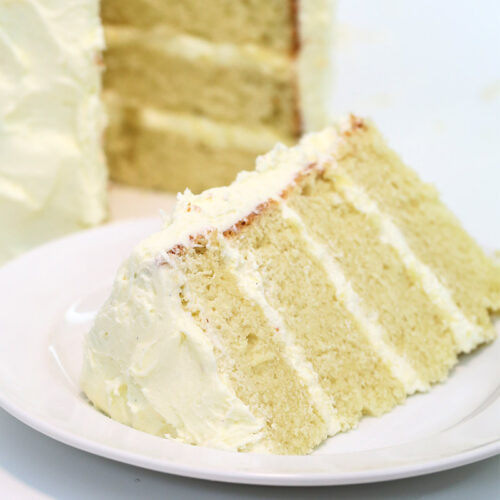 The vanilla bean cake has been sliced. The slice sits on a white plate with the remaining cake in the background.