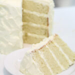 The vanilla bean cake has been sliced. The slice sits on a white plate with the remaining cake in the background.