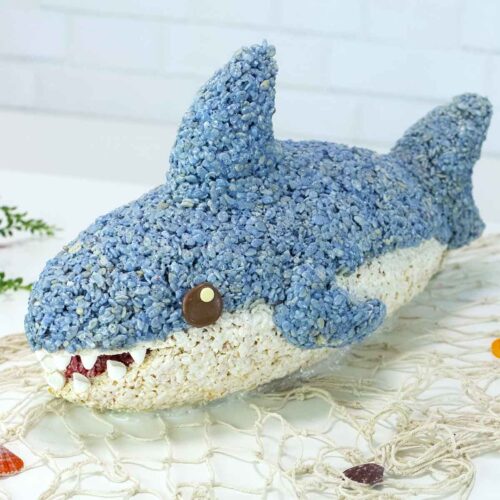 a rice krispie treat shark on a white table with a fish net and seashells