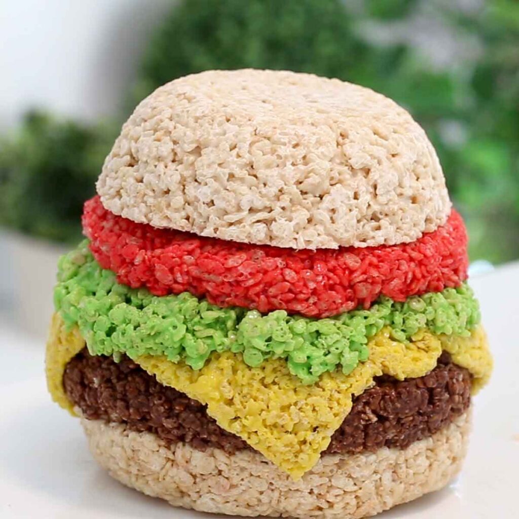 a burger made from cereal treats on a white table with greenery in the background