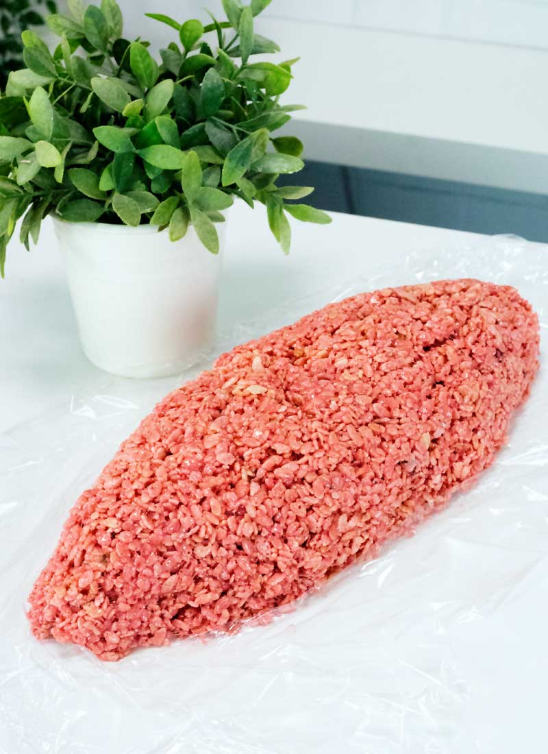 An oval-shape red rice krispie treat on a white table with a green plant