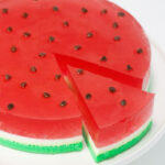 A circle of red, green and white watermelon jello is on a white tray with a slice cut out.