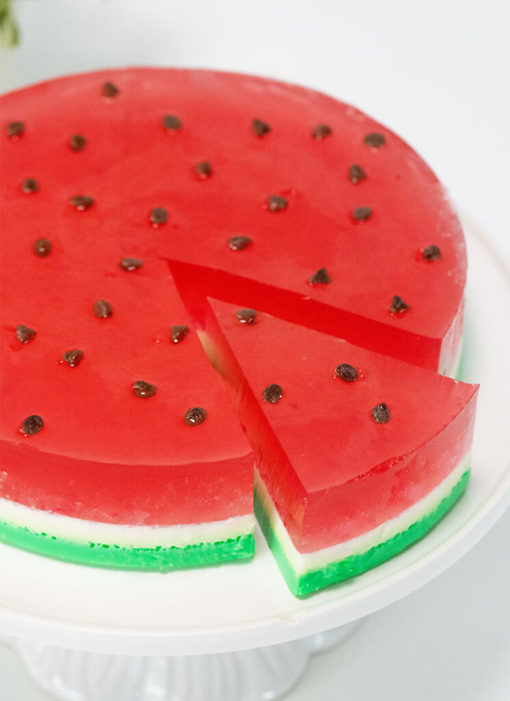 A circle of red, green and white watermelon jello is on a white tray with a slice cut out.