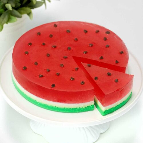 A round jello watermelon with a slice cut out.