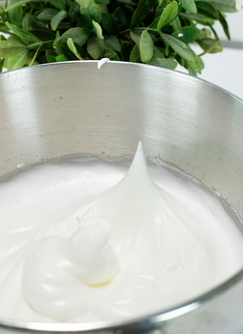 Egg whites that have been whipped to a stiff peak in a stainless steel mixing bowl.