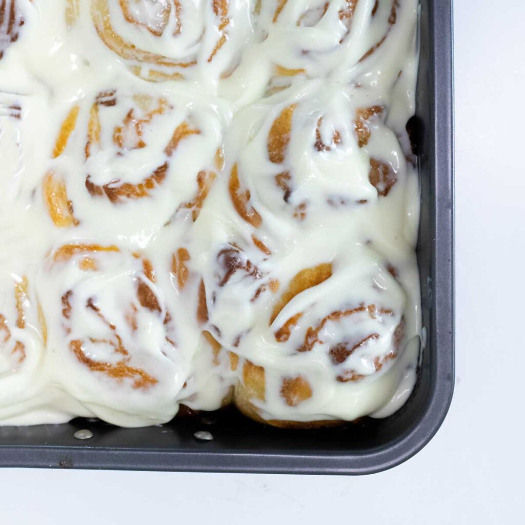 A bird's eye image of a grey baking dish filled with iced cinnamon buns.