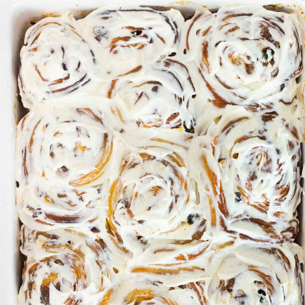 A white dish filled with iced cinnamon rolls.