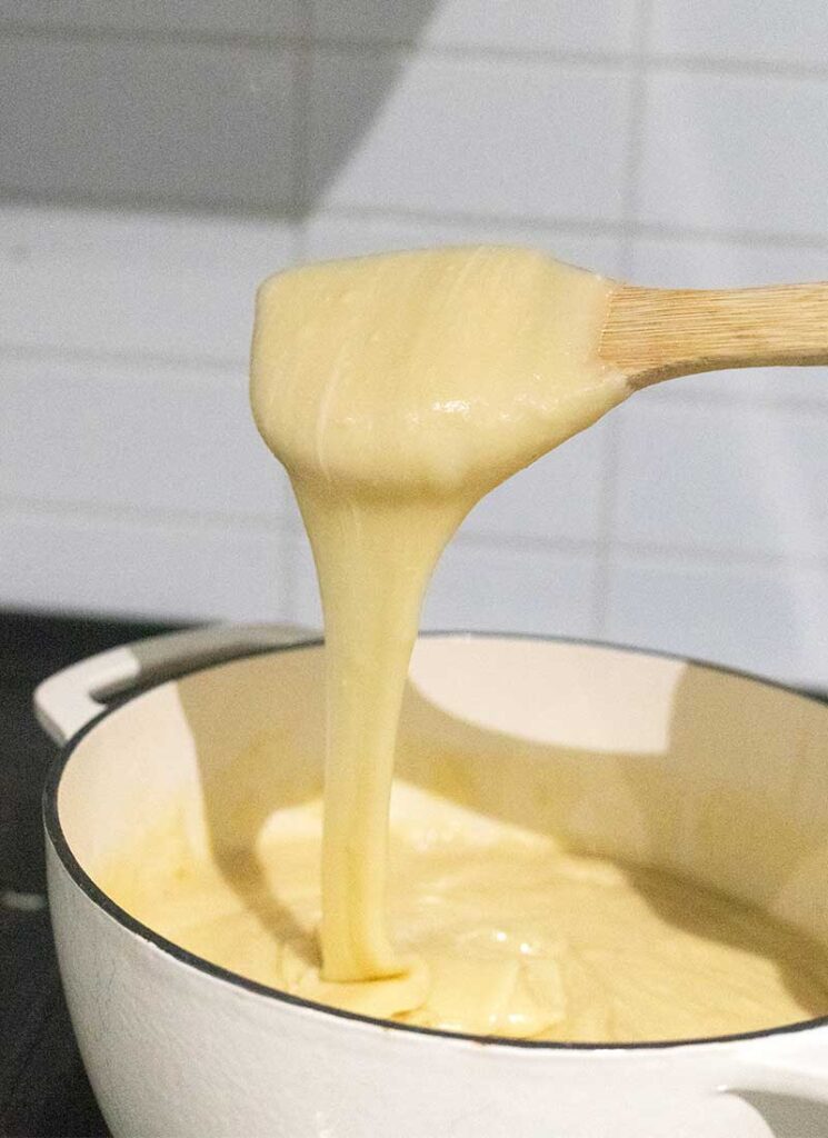 Thick, white fudge is dripping from a wooden spatula into a white pot sitting below.