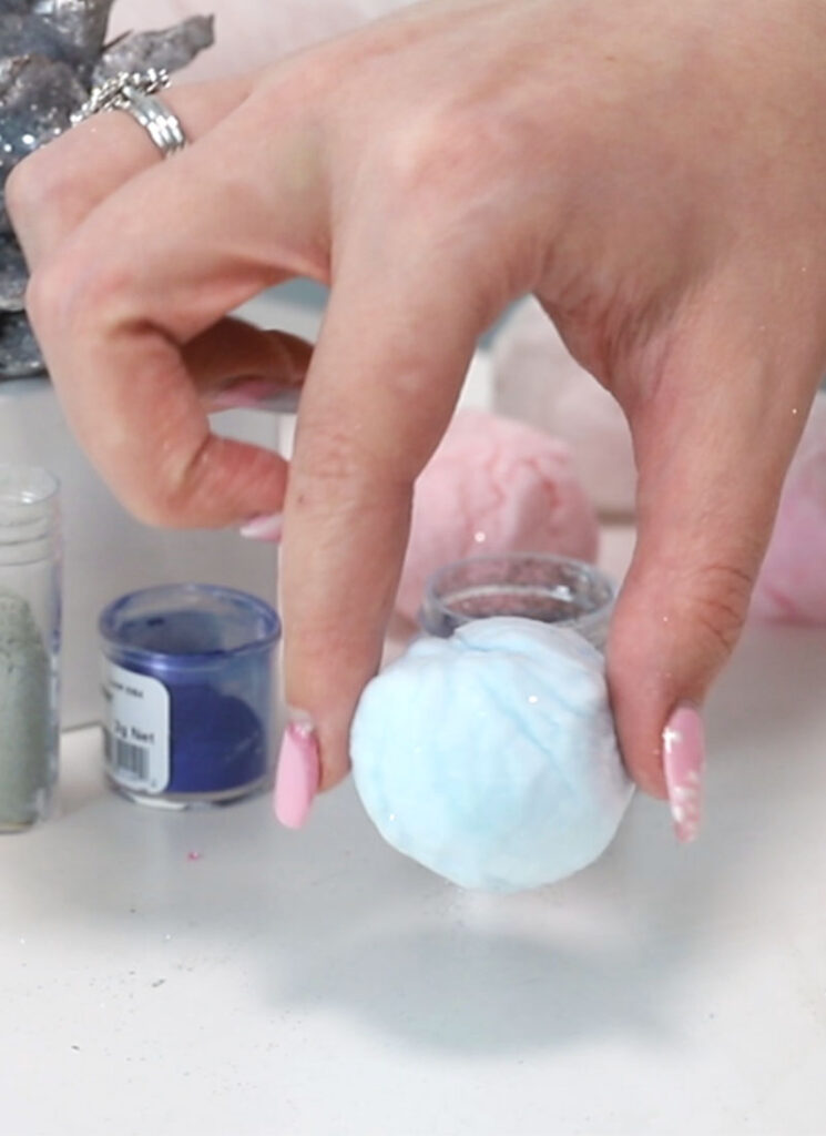 A hand is holding a ball of blue cotton candy between two fingers.