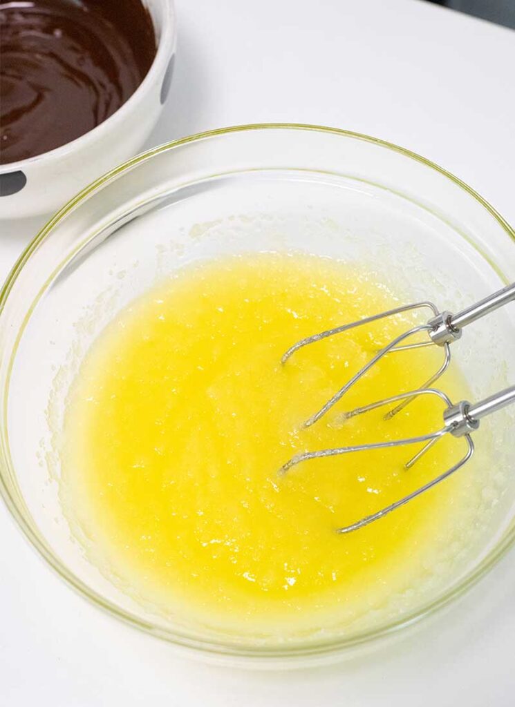Sugar and melted butter have been combined and are in a glass bowl with metal whisks.