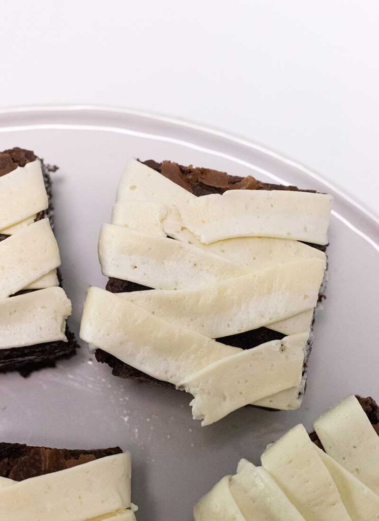 Brownie squares have been decorated with white buttercream to look like mummy bandages.