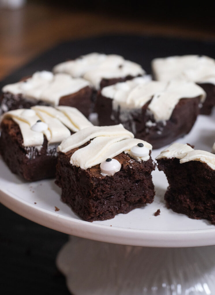 A side view of mummy brownies on a white plate. One of the brownies has been broken in half.