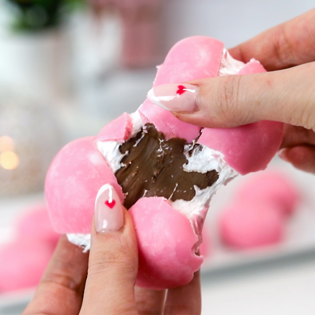 A pink chocolate heart is being pulled apart, revealing the marshmallow and nutella filling.