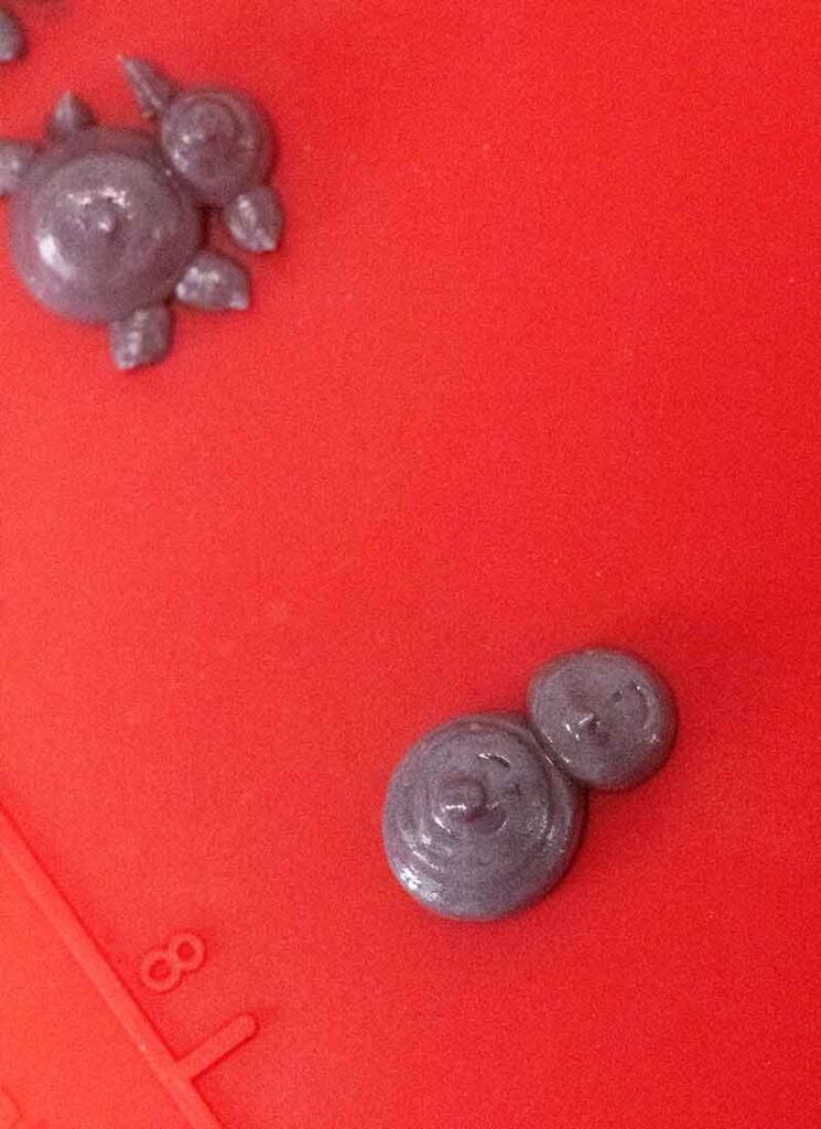 A close up of a red silicone baking mat. Black royal icing spiders have been piped onto the mat.