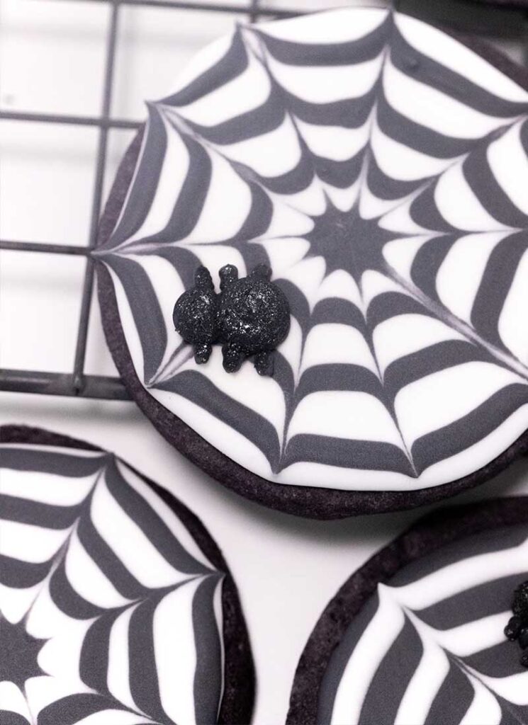 A close up of a spider web cookie. A sparkly spider is on the cookie.