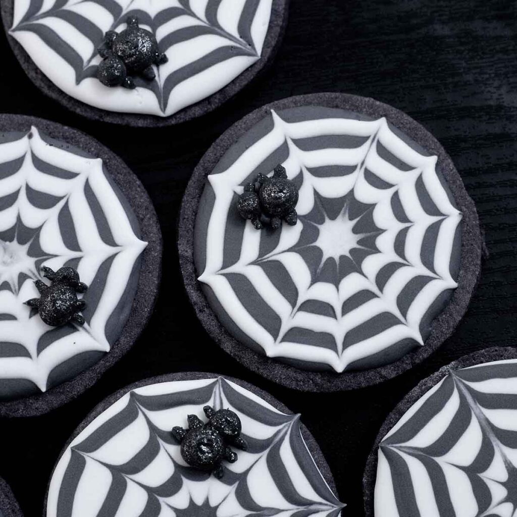 A top down view of the spider web cookies on a flat black table.