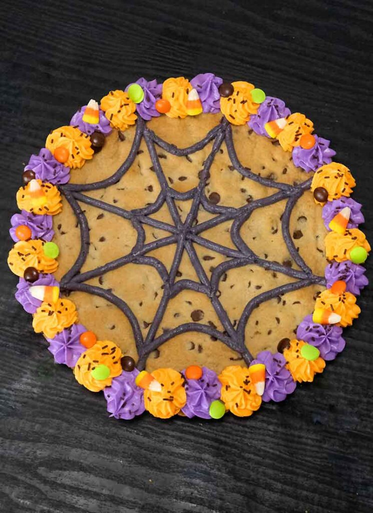 A top down view of the Halloween cookie cake. It is on a black table with skeleton hands reaching for the cookie from the top left.