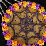 A top down view of the Halloween cookie cake. It is on a black table with skeleton hands reaching for the cookie from the top left.