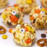 The popcorn balls are scattered on a white surface, surrounded by pretzels and Halloween candy.