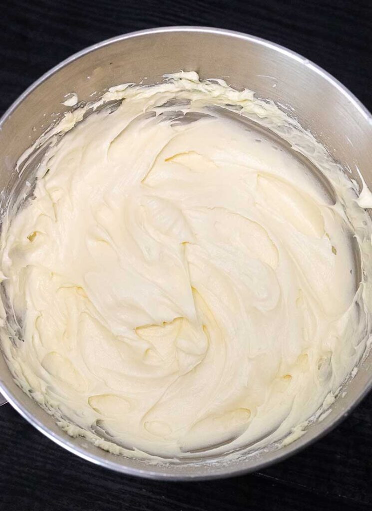 A top down view of an steel mixing bowl containing freshly make white cream cheese frosting.